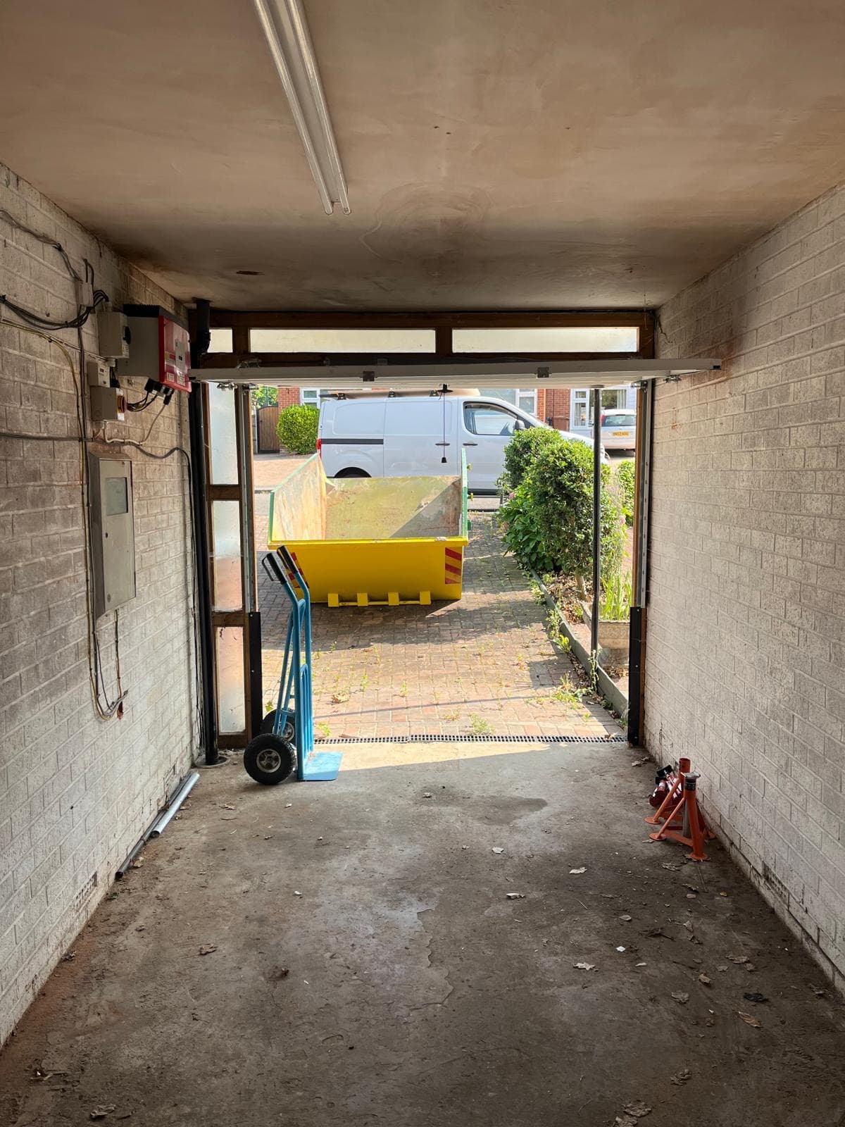 Looking out of an emptied garage through the open door towards a skip and a van on the drive