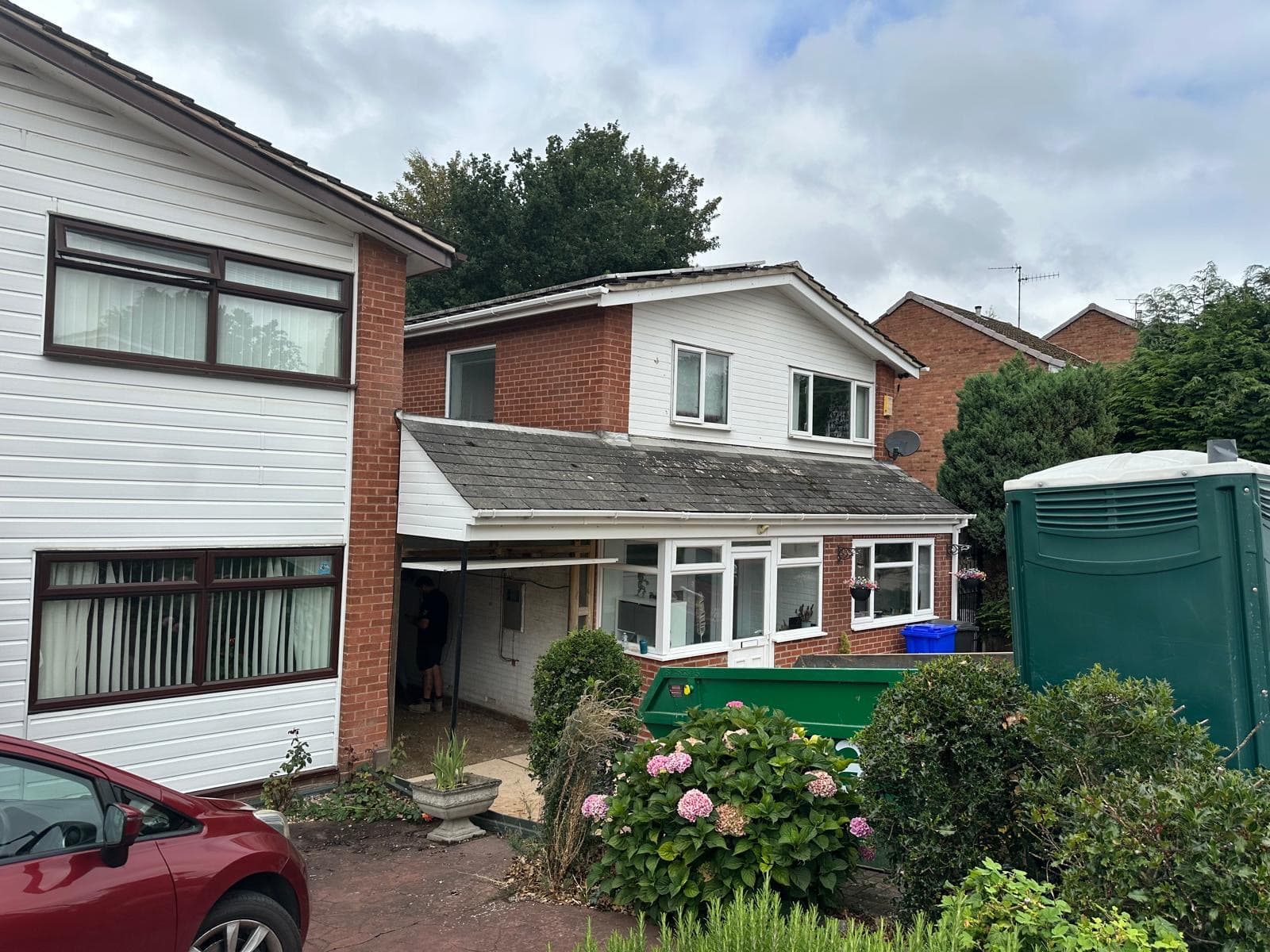 The house with the garage door removed and the opening framed in new timber, with a skip and site toilet outside