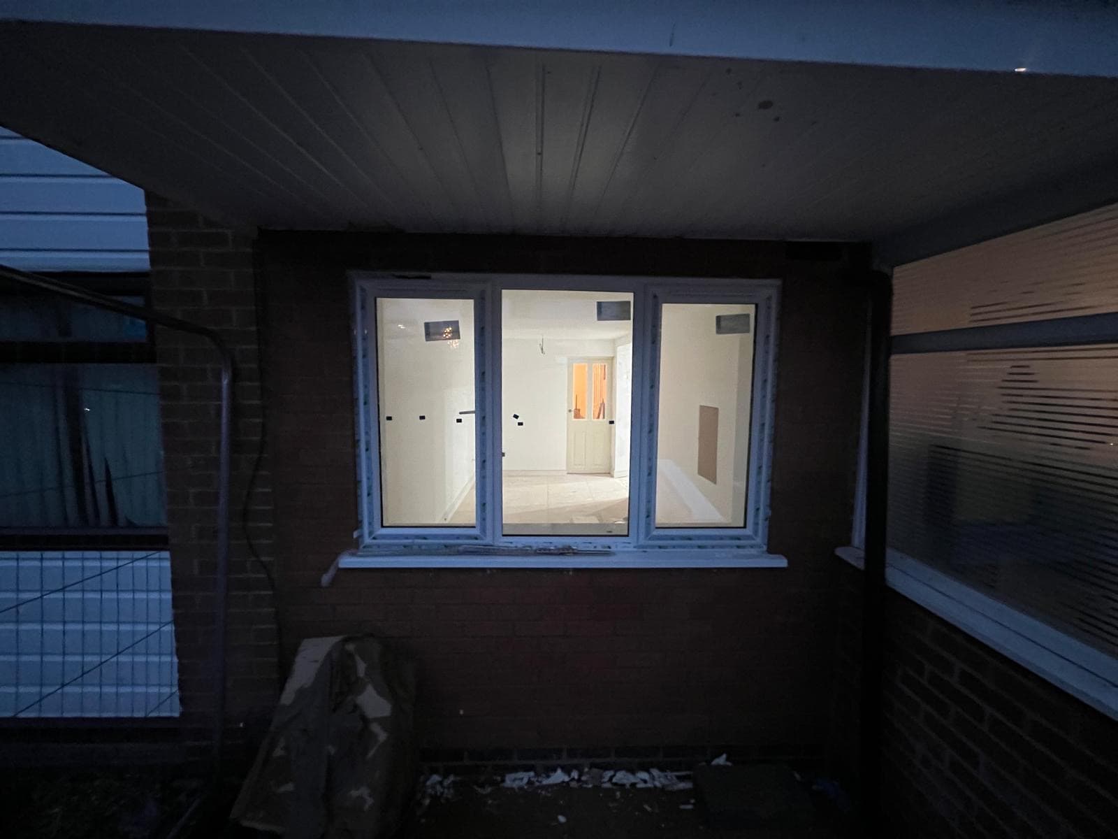 The new window seen from outside at dusk, with the finished plaster and internal door visible through the glass