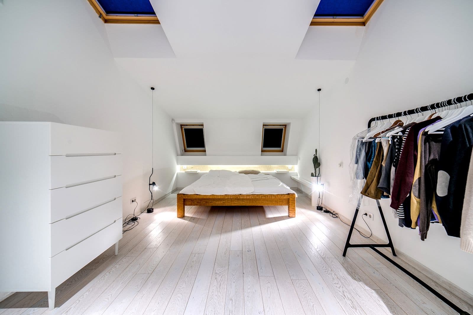 A converted loft bedroom with rooflights, white walls and a pale timber floor