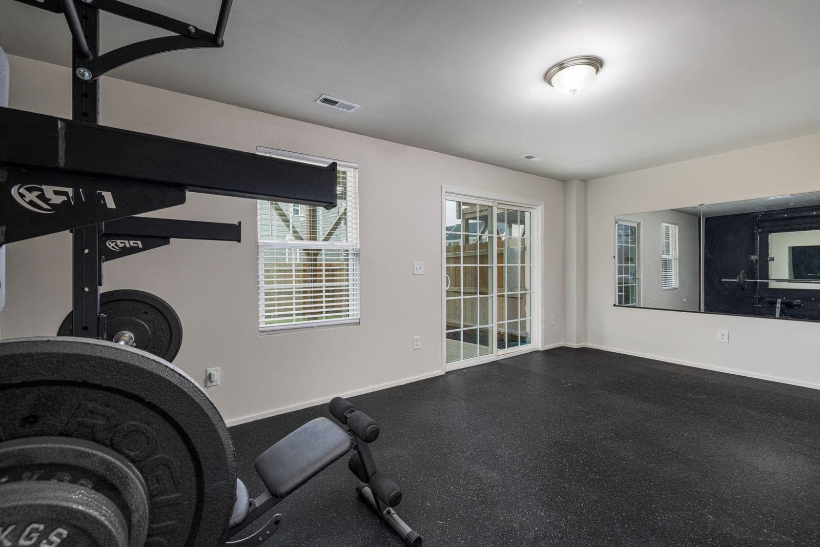 A home gym with rubber flooring, a weights rack and bench, and a mirrored wall