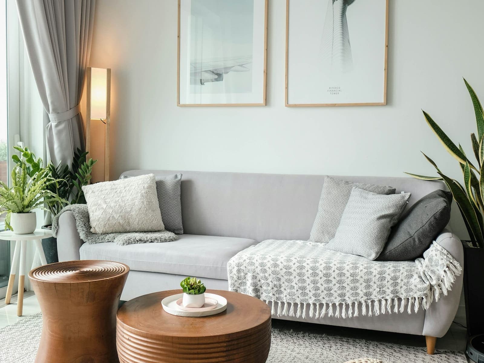 A light living room with a grey sofa, wooden side tables, plants and framed prints