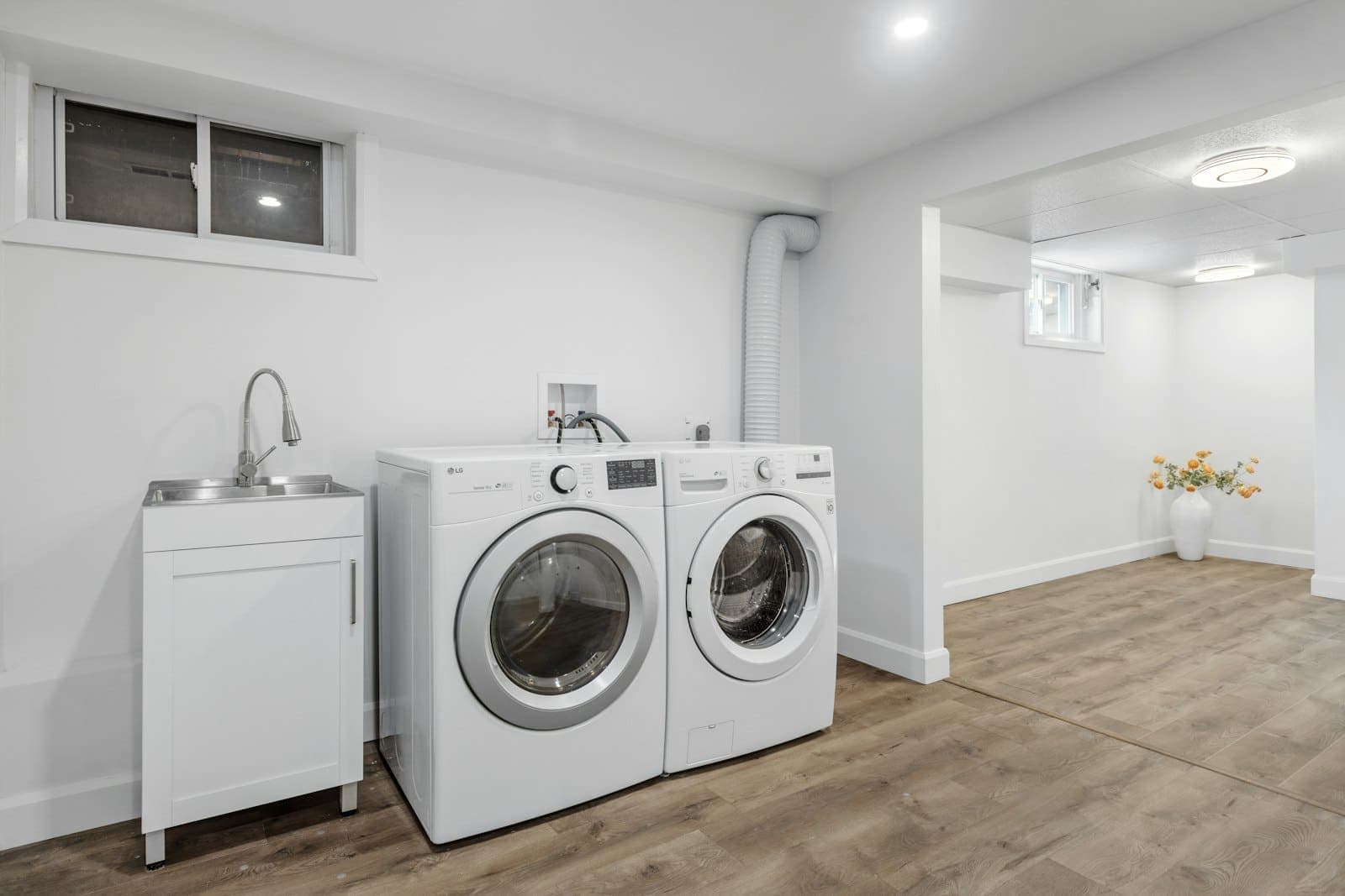 A bright utility room with a washing machine, a tumble dryer and a utility sink