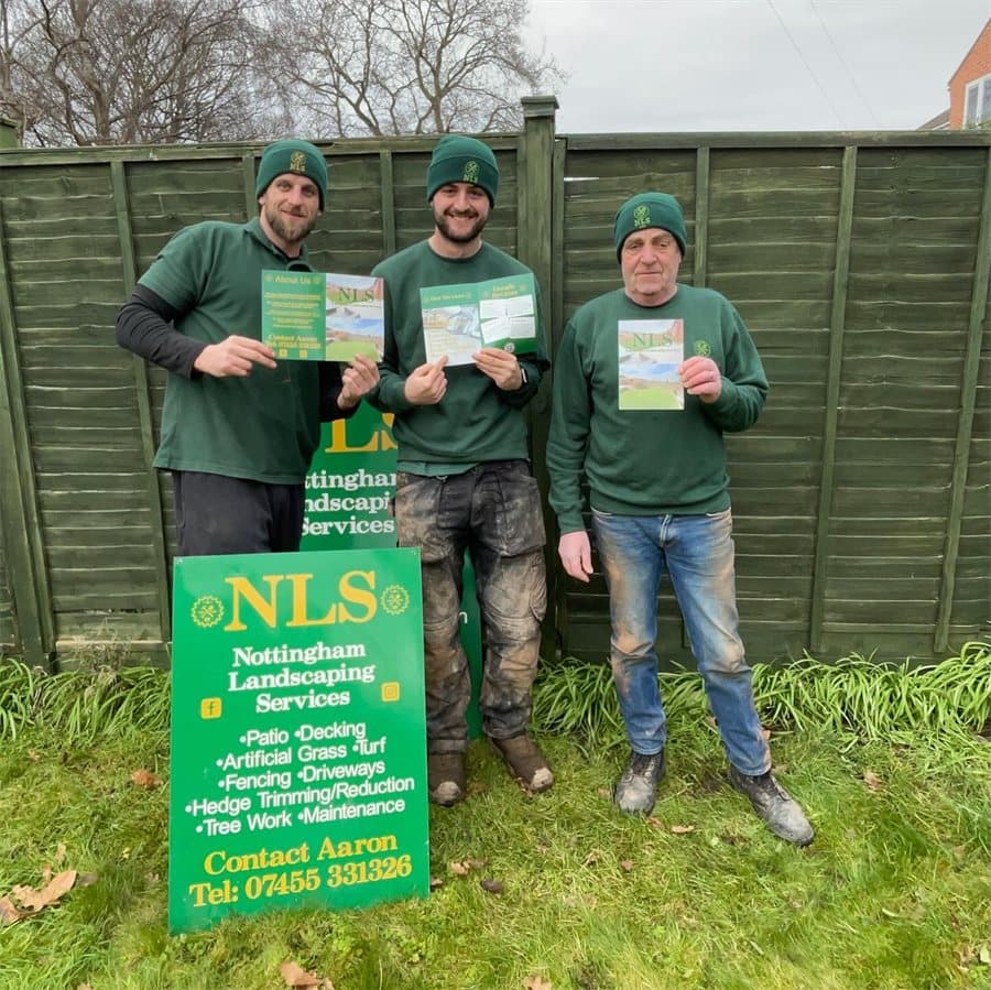 Three of the NLS team holding company leaflets beside the NLS sign