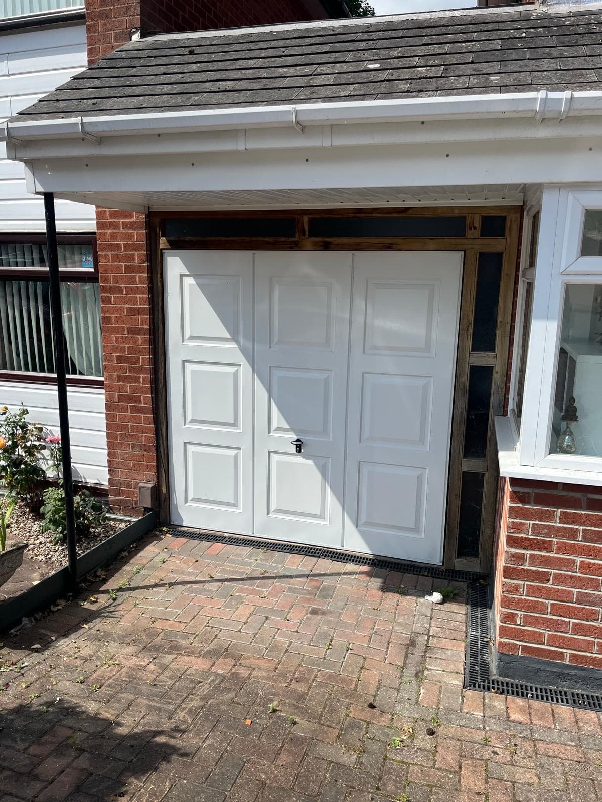A white up-and-over garage door set in a red brick opening beneath a tiled roof